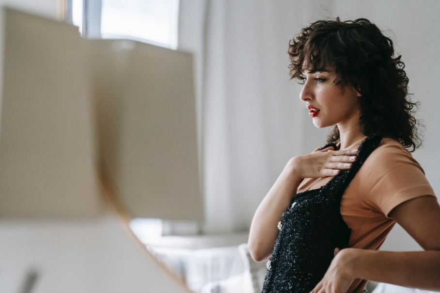 melancholic-woman-trying-on-wear-while-reflecting-in-mirror-indoors