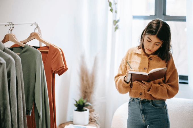 ethnic-employee-writing-in-journal-against-various-wear-in-house