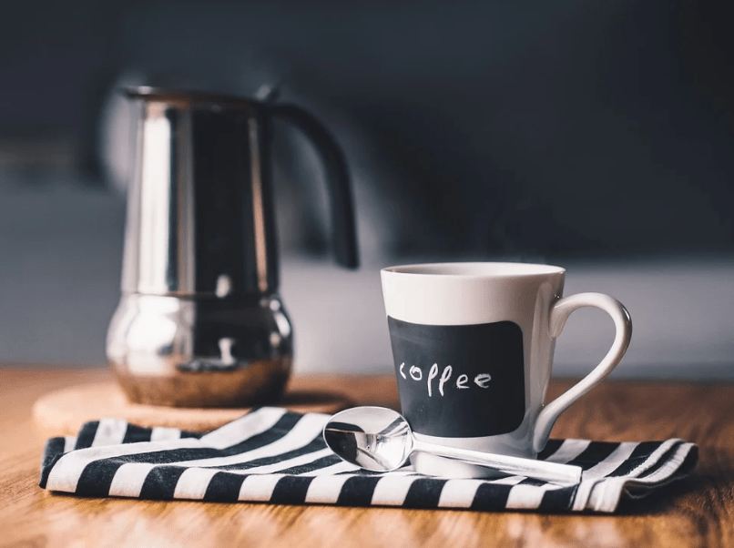 An image showing a cup of coffee with a coffee maker in the background.