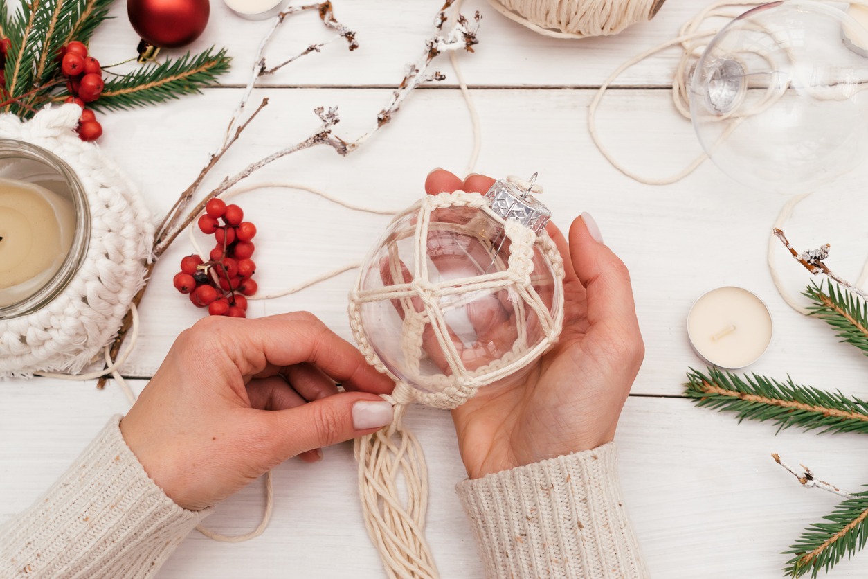 A woman decorates a transparent Christmas ball with macrame-style weaving, handmade decor in eco-style, hands close-up, top view