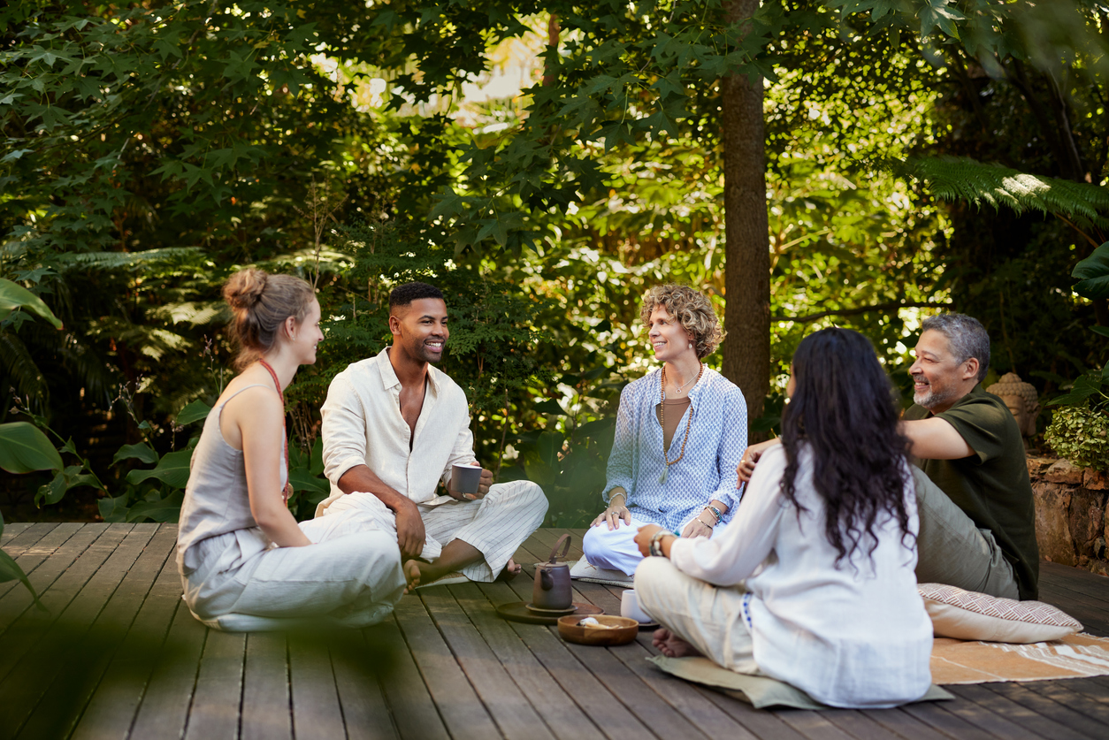 Group of diverse people enjoying each other's company while sitting outdoors at a peaceful wellness retreat