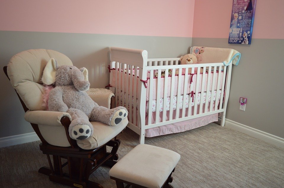 a simple baby room with a white wooden crib and rocking chair with stuffed toys