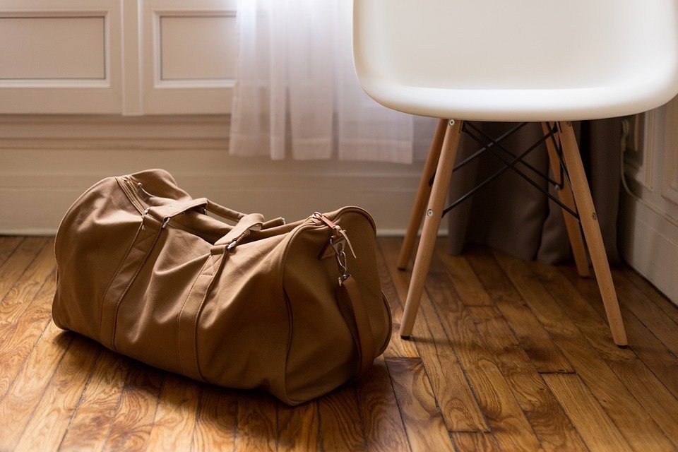 a brown luggage bag beside a chair on a wooden floor