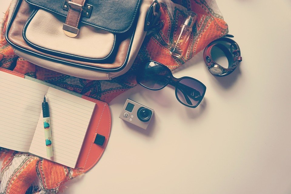 a bag with a camera, notebook, sunglasses, watch, and scarf