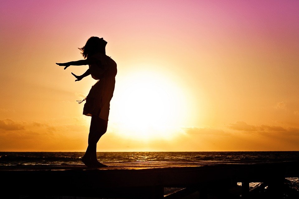 silhouette of a woman feeling the air by the beach at sundown