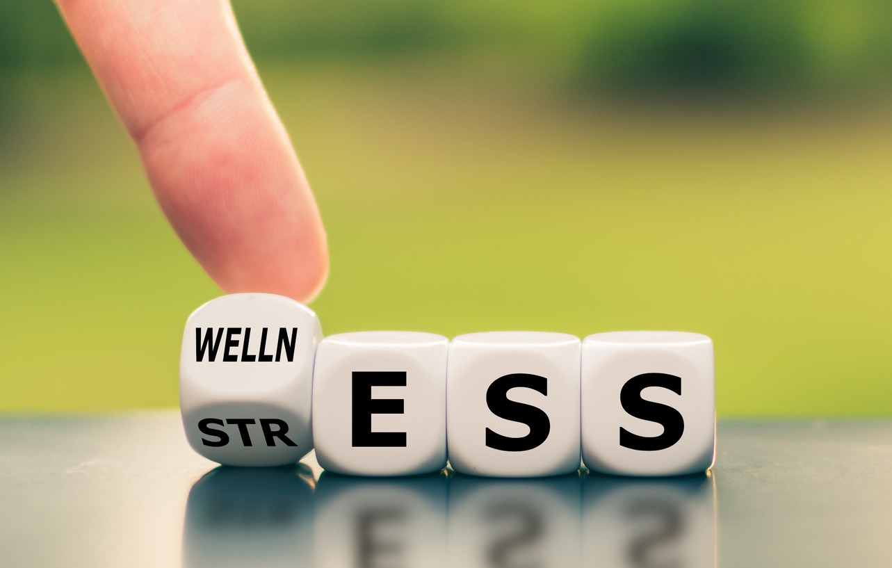 Wellness instead of stress. Hand turns a dice and changes the word "stress" to "wellness".