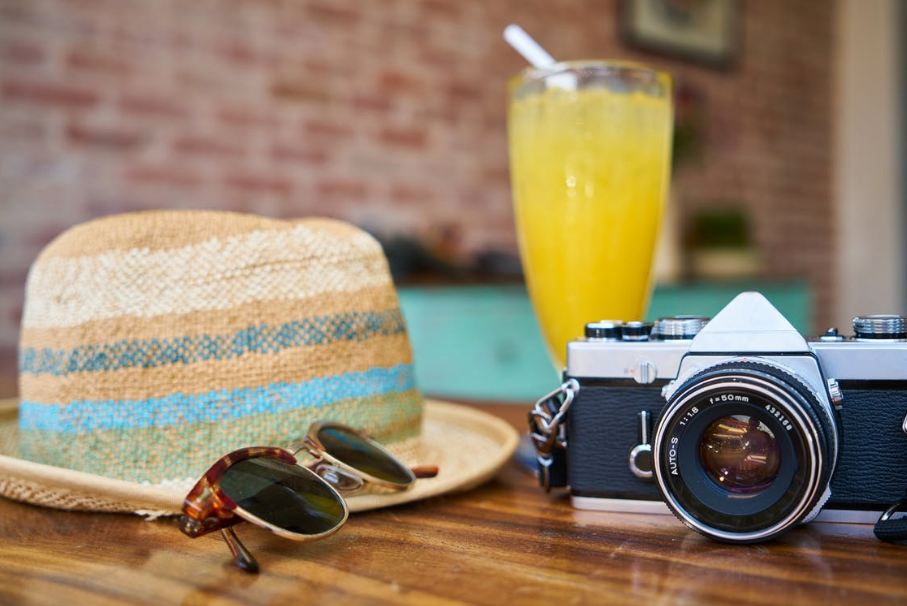 A black DSLR camera with a glass of juice, hat, and sunglasses