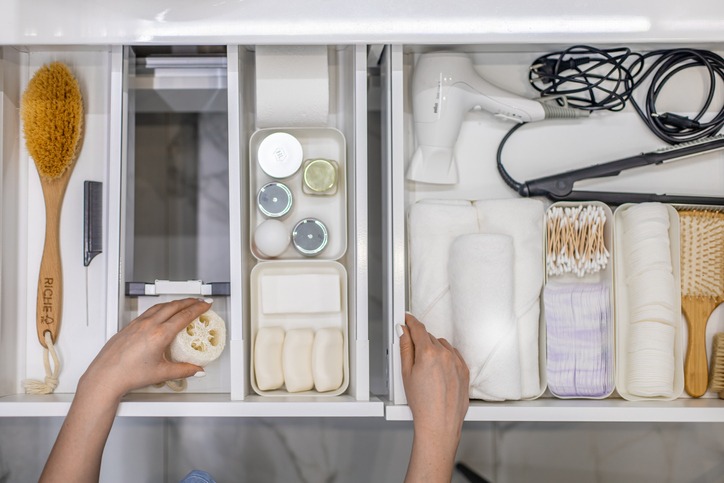 Top view of woman hands neatly organizing bathroom amenities and toiletries in drawer in bathroom