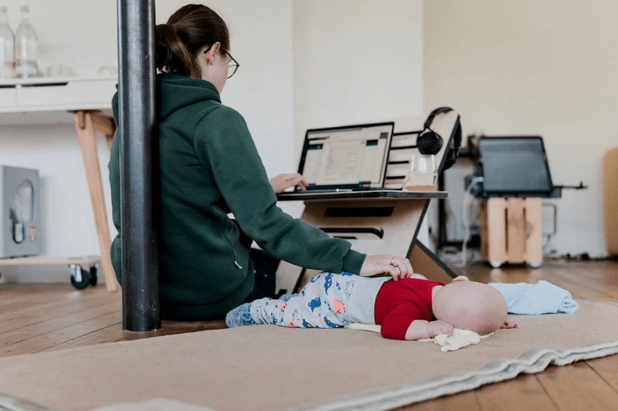 An image showing a woman cradling a baby while working at her laptop.