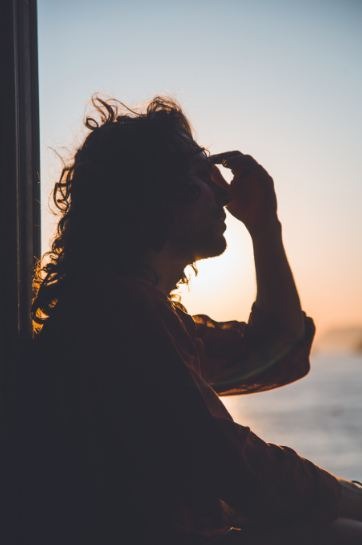 A person holding their forehead against a sunset background.