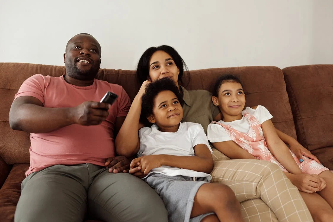 Family Sitting on a Brown Couch Watching TV